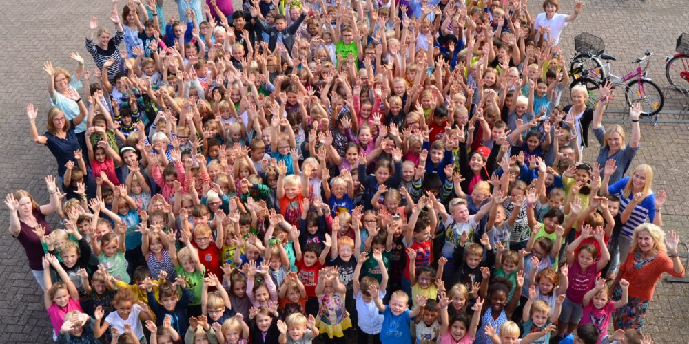 Schülerinnen und Schüler winken gemeinsam auf dem Schulhof