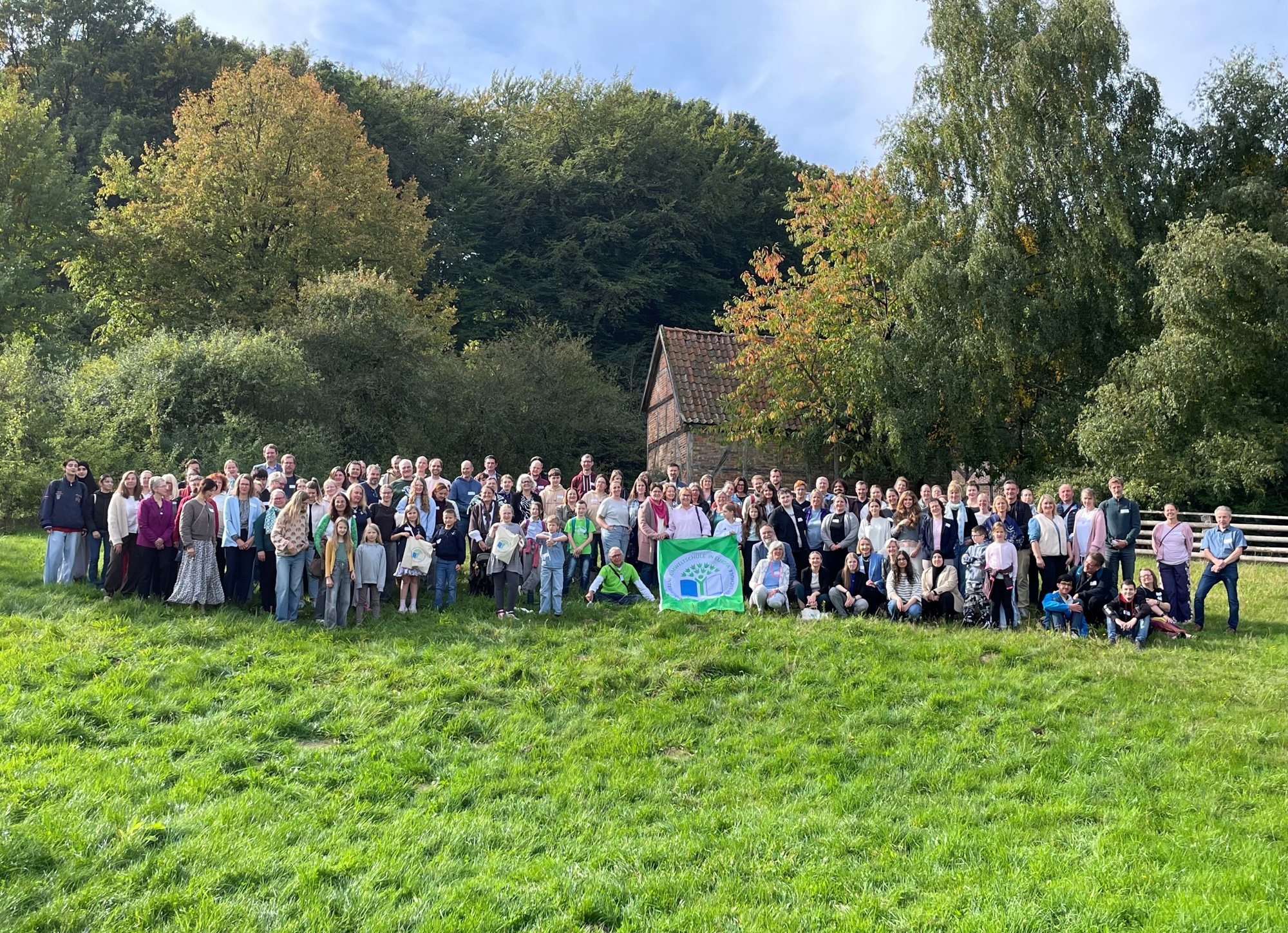 Großes Gruppenfoto auf einer Wiese vor einem alten Fachwerkhaus: Vertreterinnen und Vertreter der ausgezeichneten Schulen mit der grünen Flagge von Umweltschule in Europa