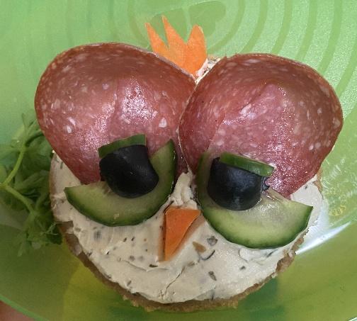 Ein belegtes Brot, mit Wurst, Gurke und Oliven als lustiges Gesicht gestaltet