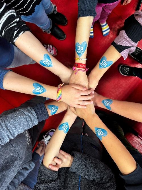 Viele Kinderhände übereinander, auf den Armen kleine blaue Herzen